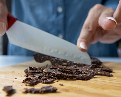 Person cutting chocolate pieces on a wooden board with a knife.